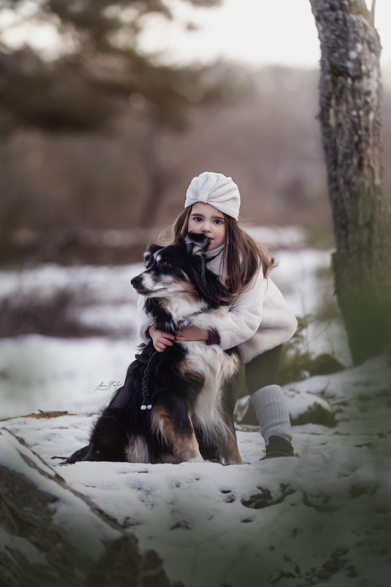 Kleines Mädchen umarmt ihren Hund im Schnee